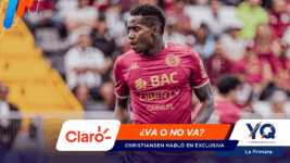 Soccer player in a maroon kit on the pitch, with a colorful news banner across the bottom reading '¿VA O NO VA? Christiansen habló en exclusiva' and logos Claro and YQ in view.