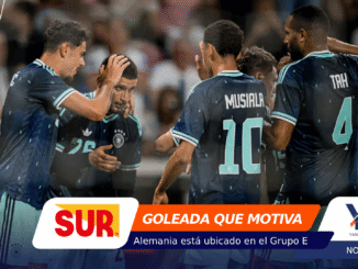 Group of soccer players in blue uniforms celebrate on the field, heads close in a moment of encouragement.