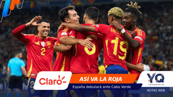 Spain national team players celebrate a goal, embracing in red jerseys on the field with a cheering crowd in the background.