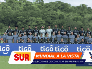 Group of soccer players posing for a team photo on the field, gray/black kits, with blue 'tigo' banners in front.