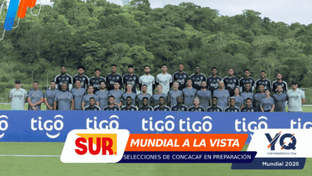 Group of soccer players posing for a team photo on the field, gray/black kits, with blue 'tigo' banners in front.