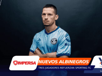 Portrait of a man in a light-blue jersey with arms crossed, standing against a dark gradient backdrop with colorful graphic overlays at the left and bottom edges, including sponsor logos.