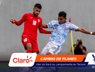 Two soccer players clash for the ball during a match: one in a red kit (#10), the other in a light blue patterned kit (#20) near a yellow post.