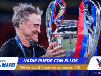 Man with gray hair smiles while holding a large silver trophy with blue and red ribbons during a celebration, stadium in the background.