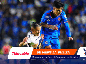 Two soccer players contesting the ball in a stadium, blue team versus white, with a sponsor banner at the bottom.
