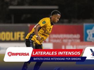 Soccer player in a yellow jersey running on the field with sponsor boards in the background during a night match, bib and logos visible on uniform.