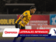 Soccer player in a yellow jersey running on the field with sponsor boards in the background during a night match, bib and logos visible on uniform.