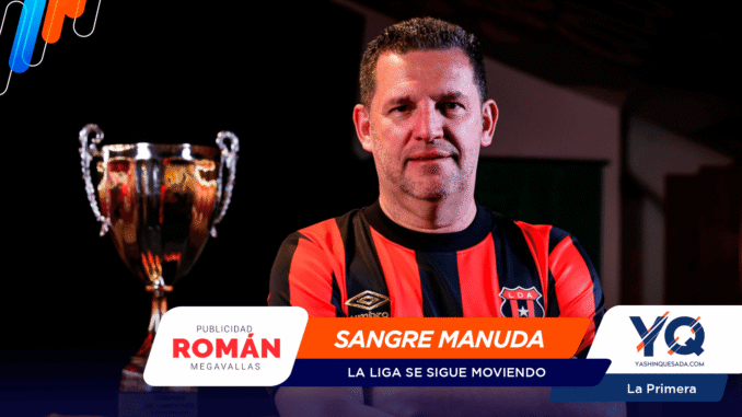 Portrait of a man in a red-and-black striped soccer jersey standing beside a silver trophy; sponsor banners cover the lower part of the image.