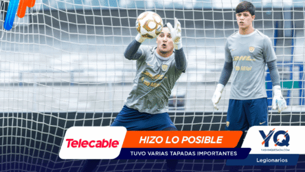 Two soccer goalkeepers in gray uniforms stand inside the goal net, one reaching for a ball, with sponsor banners across the bottom of the image