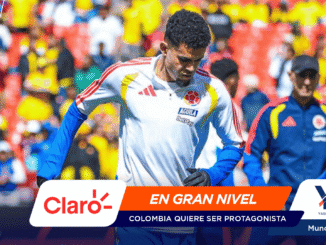 Colombia soccer player in a white jersey with crest and blue sleeves, amid a colorful stadium crowd; banner shows Claro and 'EN GRAN NIVEL' for Mundial 2026