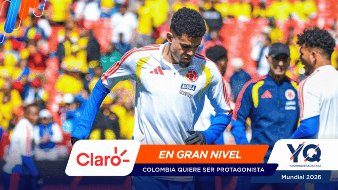 Colombia soccer player in a white jersey with crest and blue sleeves, amid a colorful stadium crowd; banner shows Claro and 'EN GRAN NIVEL' for Mundial 2026