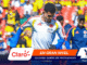 Colombia soccer player in a white jersey with crest and blue sleeves, amid a colorful stadium crowd; banner shows Claro and 'EN GRAN NIVEL' for Mundial 2026