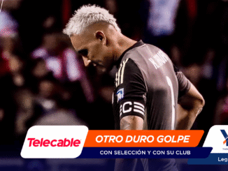 Soccer player with bleached hair in a dark jersey on the field; foreground shows sponsor banners 'Telecable' and 'OTRO DURO GOLPE' across the bottom.