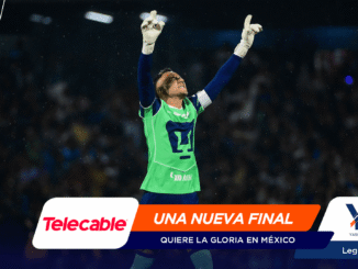 Soccer goalkeeper in a neon-green kit raises both arms in celebration on the pitch, with sponsor banners across the bottom edge.