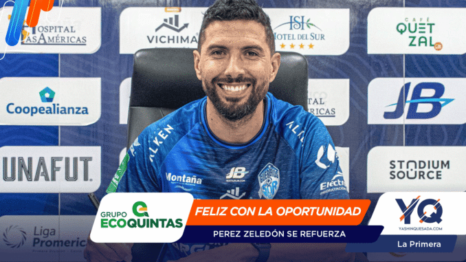 Smiling male athlete in a blue jersey seated at a press conference backdrop with sponsor logos behind him.
