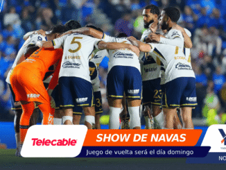 Soccer team huddling in a blue stadium, players in white and navy uniforms with orange goalie, banners at bottom display sponsors like Telecable and YQ Vivans.