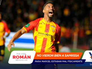 Soccer player in red and yellow jersey celebrates with mouth open on a blurred stadium background; foreground has sponsor banners.