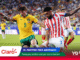 Two soccer players compete for the ball in a crowded stadium, with colorful banners and Claro/Mundial 2026 branding along the bottom of the image.