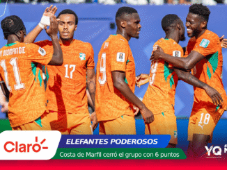 Ivory Coast football players in orange jerseys celebrate together on the field with a blue stadium backdrop and sponsor graphics at the bottom.