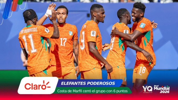 Ivory Coast football players in orange jerseys celebrate together on the field with a blue stadium backdrop and sponsor graphics at the bottom.