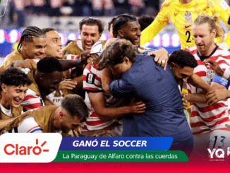 Soccer players in red-and-white striped uniforms celebrate in a tight huddle on the field after a goal