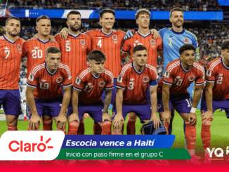 Group photo of the Colombian national football team posing on the field before a match, in red jerseys and blue shorts, with a crowded stadium in the background.