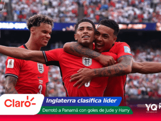 Three England footballers in red jerseys celebrate a goal on the pitch as a packed stadium cheers in the background.