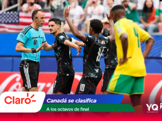 Soccer players celebrate together near a referee on a crowded field, with colorful banners in the foreground and a Coca‑Cola ad visible behind them.