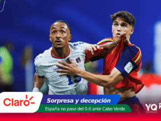 Two soccer players clash for the ball during a match: one in white and blue, the other in red and blue, with colorful sponsor banners at the bottom.