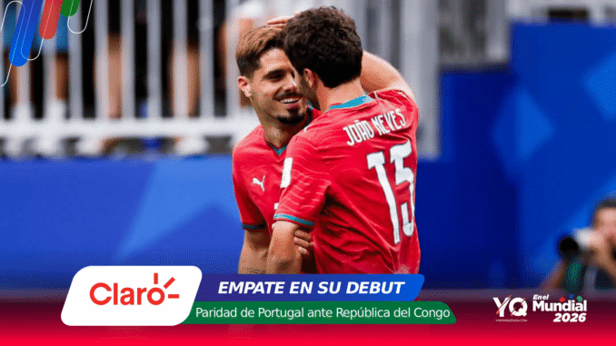 Two soccer players in red jerseys celebrate a moment on the field, hip-to-hip and smiling, with blue stadium backdrop and sponsor banners at the bottom.