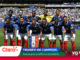Equipo de fútbol de Francia posa para una foto de victoria en un estadio lleno, con pancartas y anuncios publicitarios alrededor (Triunfo de Campeón).