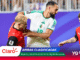 Soccer players in red and white compete for the ball on a purple advertising background in a stadium.