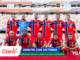 Norwegian football team in red-blue jerseys posing for a group photo on a stadium pitch, with a cheering crowd and colorful sponsor banners overlay.