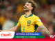 Australian soccer player in yellow jersey celebrates with arms outstretched, smiling