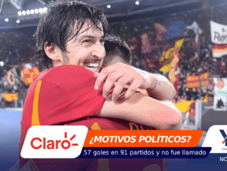 Two soccer players hug on a crowded stadium field after a match, celebrating a win: the scene is full of fans and banners in the background.