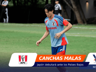 Young male soccer player in a light blue Japan jersey with red accents runs on a grassy field; foreground shows sponsor banners including KFC and 'CANCHAS MALAS'.