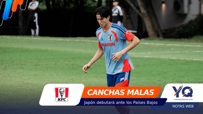 Young male soccer player in a light blue Japan jersey with red accents runs on a grassy field; foreground shows sponsor banners including KFC and 'CANCHAS MALAS'.