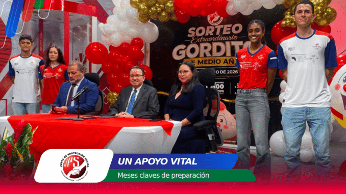 Panel of six people seated or standing behind a red-and-white table during a formal event, with colorful balloons and a backdrop banner in Spanish that reads 'SORTEO EXTRAORDINARIO' and 'UN APOYO VITAL'.