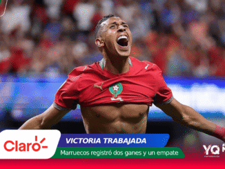 Moroccan footballer celebrating a goal with arms outstretched in a red jersey, stadium crowd in the background.