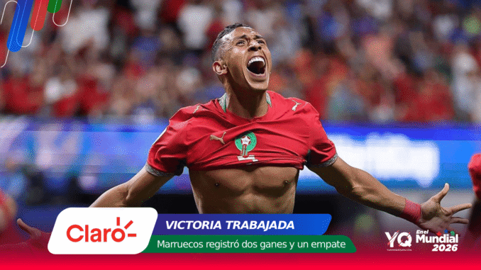 Moroccan footballer celebrating a goal with arms outstretched in a red jersey, stadium crowd in the background.