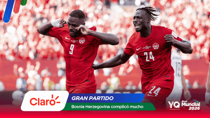 Two Canadian soccer players in red celebrate a goal on the field as a cheering crowd looks on, with sponsor banners at the bottom of the image.