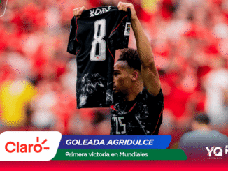 Soccer player raises a black jersey numbered 8 amid a red-clad stadium crowd, with Claro and Mundial 2026 banners.