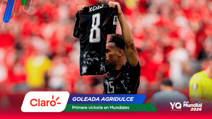 Soccer player raises a black jersey numbered 8 amid a red-clad stadium crowd, with Claro and Mundial 2026 banners.