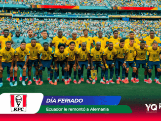 Ecuador national soccer team wearing yellow jerseys and blue shorts posing for a group photo on the pitch with a full stadium in the background.
