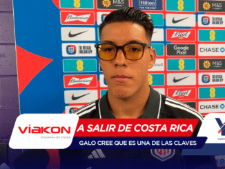 Man wearing black-rimmed glasses being interviewed at a press conference in front of a colorful sponsor backdrop.