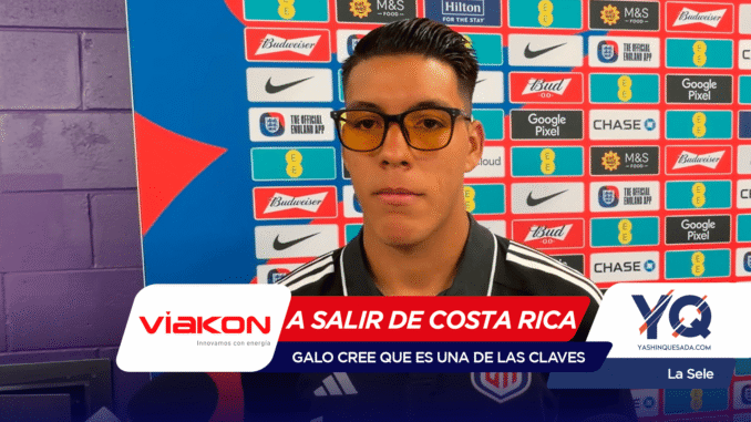 Man wearing black-rimmed glasses being interviewed at a press conference in front of a colorful sponsor backdrop.
