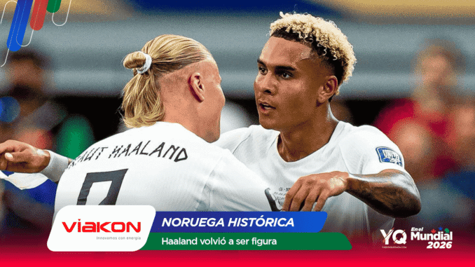 Two footballers in white jerseys embrace in a celebratory moment on the field, with sponsor banners and text overlays in the foreground.