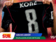 Soccer player holds up a black jersey with the large number 8 and the name KONÉ on it.