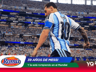 Soccer player in a blue-and-white striped jersey on a packed stadium field with Roma and Mundial 2026 banners in view.