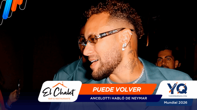 Close-up of a man with curly hair and beard, wearing sunglasses and earrings, at a dark event with orange-blue promotional banners reading 'PUEDE VOLVER' in the foreground.